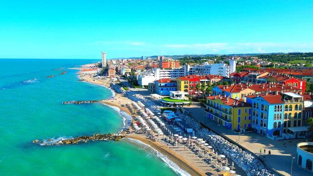 Beautiful aerial truck left pan right shot from Porto Recanati, from a side view of the Adriatic Sea splashing on the shore to a frontal view of the beach with colored buildings and peaceful hills