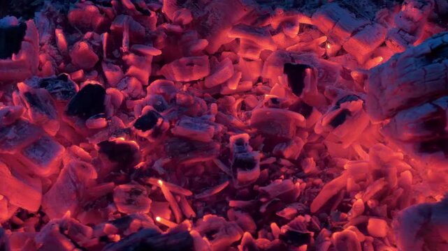 Panning over red hot coals glowing and flickering in a wood fire in 4K footage