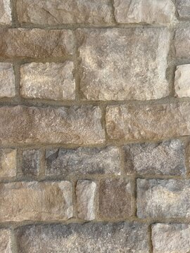 Macro close-up of natural stacked irregular fieldstone masonry wall with grey and brown tones and rough texture