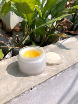 Open white cosmetic jar with yellow skincare balm in sunlight. Not AI-generated.