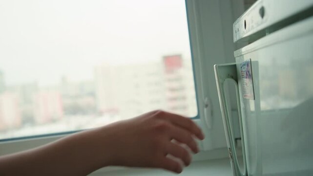 Fridge handle left after cooking, empty closeup of refrigerator handle with small magnet note, sunlit window view, still domestic scene, implied departure of apartment cook after quick meal, quiet