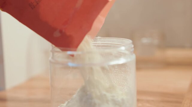 Jar filling with flour for sourdough starter, artisan chef prepping on rustic wooden counter, fine powder cascade, morning light, fermentation recipe step captured in tactile detail