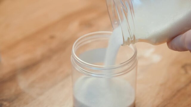 Close up hands pouring sugar jar on wooden countertop, glass container filling with fine granulated sugar, warm morning light, home baker measuring for recipe, gentle rhythmic pour, tidy kitchen