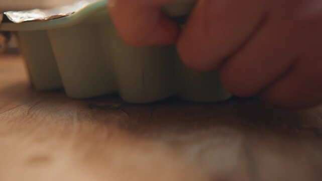 Closeup of baking tray on wooden table. Detailed view of bakery process with baking tools and surface. Detailed depiction of home baker gently pressing silicone mold on wooden surface