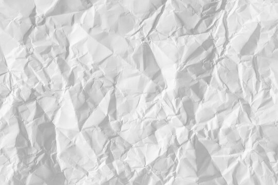 Close-up of white crumpled paper surface. This wrinkled paper texture with natural shadows is perfect for backgrounds, artistic overlays, and minimalist design projects.