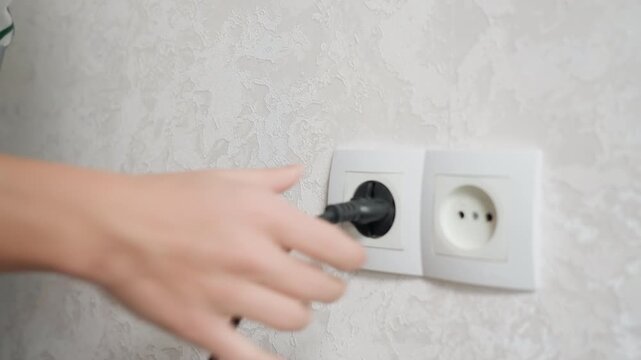Closeup scene showing hands guiding plug into electrical outlet with neat background. Focused shot of hand guiding plug into socket against neutral wallpaper background for home electrical setup