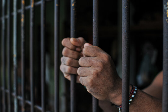 Close up of hand holding iron bar of a prison cell, representing restraint, isolation, and crime concept
