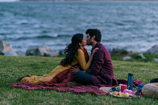 Couple kissing during a seaside picnic on a grassy shore