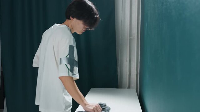 Tidy workspace maintained through disinfecting procedures. Asian individual wipes down desk to ensure cleanliness. Promptly sanitizing area to promote health and hygienic conditions