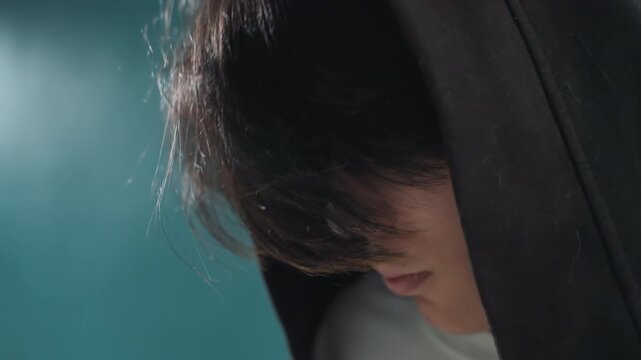 Intense hoodie photograph. Moody teal hoodie shot with emotion. Closeup of young person with fringe and soft lighting. Cinematic portrait of individual with fringe and intimate mood
