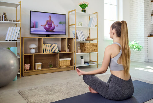 Woman yoga home online fitness tv meditation. She follows a virtual instructor on television, learning breathing and stretches for balanced workout and mindfulness. Calm wellness focus at home