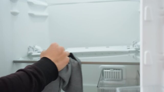 Cleaning fridge shelves. Wiping interior with microfiber cloth. Detailed cleaning of refrigerator shelf with microfiber towel. Closeup of domestic fridge cleaning focusing on shelf and cloth movement