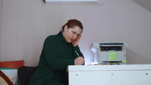 Individual laboring anxiously at desk. Person tirelessly managing chaos and mounting workload stresses. Independent worker battling fatigue and pressure in cluttered home environment