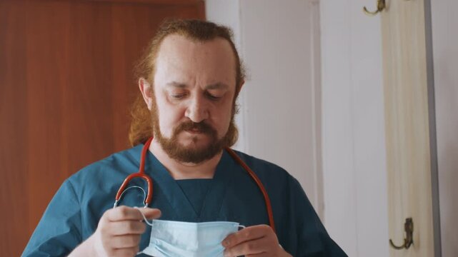 Paramedic removing mask after home consultation, clinician checks notes and reflects, stethoscope resting on shoulders, thoughtful tired expression, indoor hallway setting with warm tones, end