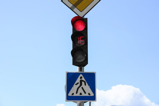 Red traffic light with countdown timer and pedestrian crossing sign against a clear blue sky, Red traffic light with a digital countdown timer showing 16 seconds, indicating a stop for vehicles