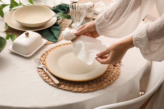 Womans hands setting a dining table with a white napkin and woven placemat for a meal or special occasion