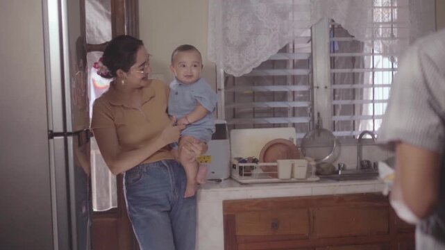 Mother holding son while father washes dishes