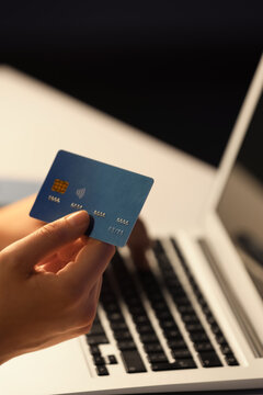 Young woman with credit card using laptop for online shopping at table in evening, closeup