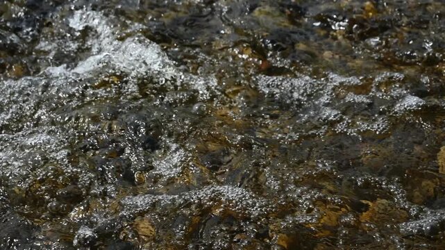 Close-up of water in a shallow stream flowing and bubbling over brown colored pebbles