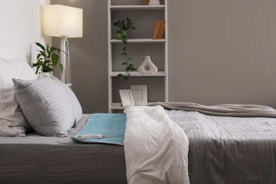 Electric heating pad with controller on bed in room