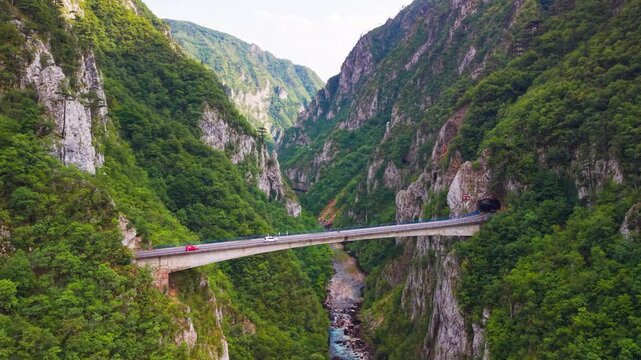Aerial view of cars driving across a bridge into a rock tunnel in Piva River canyon near Montenegro border