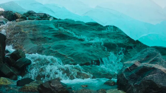 Close-up footage filmed inside a crevice beneath Nigardsbreen Glacier in Norway. Meltwater drips and flows through the ice, revealing the vivid blue tones and textured interior of the glacier as it sl