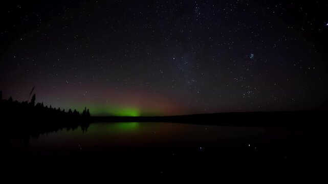 Nighttime timelapse of stars and Aurora Northern Lights above and reflecting in a large calm lake