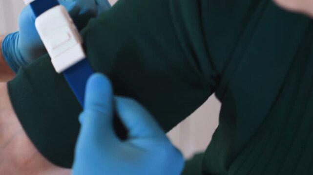 Closeup hand with blue tourniquet, nurse wearing gloves securing strap before venipuncture, polished black nails visible, calm domestic clinic, soft lighting, patient seated, medical supplies nearby