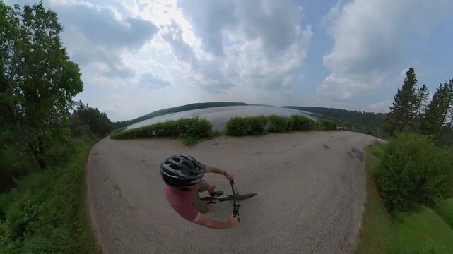 Tiny-planet view looking down on a cyclist riding along a narrow road next to a large lake