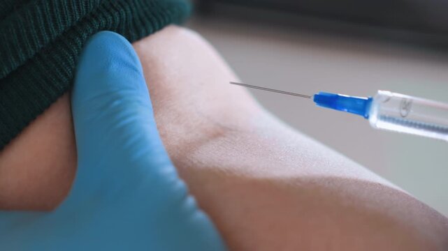 Closeup arm receiving injection by nurse, blue glove stabilizing inner elbow, syringe piercing skin for vaccination, antiseptic prep, domestic interior, gentle steady hand, professional care