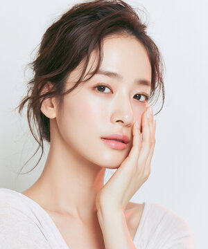 Extreme close up beauty portrait of young East Asian woman touching her flawless glowing cheek skin with natural makeup against clean bright white studio background