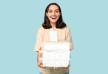 Fototapeta premium Young woman with laundry basket and bottle of detergent on blue background