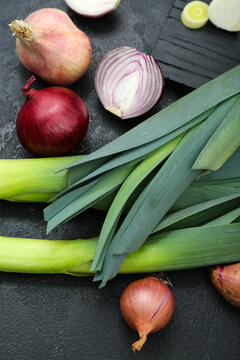 Board with different kinds of onion on grunge black background