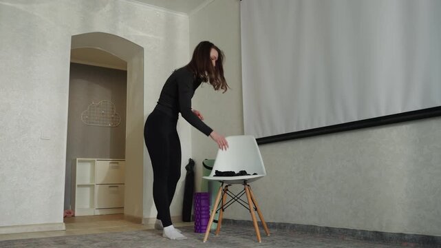 Woman picking up yoga mat and bag near doorway, carrying green rolled mat out of room, purposeful stride and indoor transition, sneakers and casual outfit, quick exit from apartment
