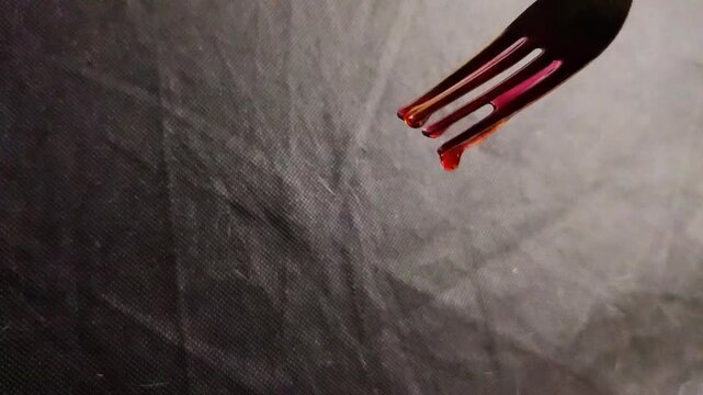 Spooky Halloween themed close up of a black fork dripping with realistic fake blood on a dark fabric background