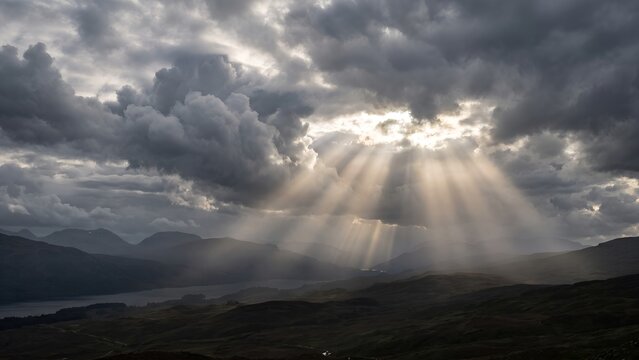Dramatic sun rays breaking through storm clouds over a dark mountain landscape.