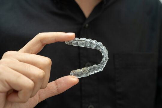 Man holding invisible aligner orthodontic retainer for dental teeth straightening.