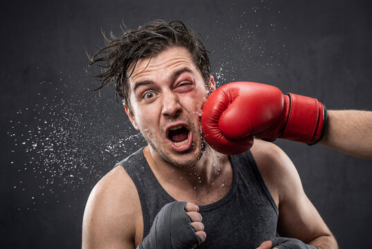 Man with a black eye getting punched in the face by a red boxing glove while spit flies