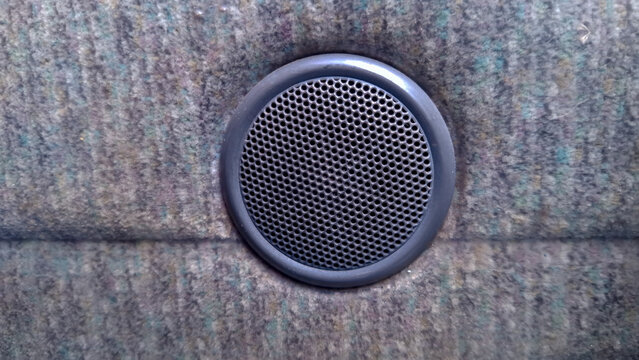 Front view close up of a circular audio speaker grille embedded into a fabric car interior door trim. Ideal for car audio systems, sound equipment, automotive interior materials, and music playback th