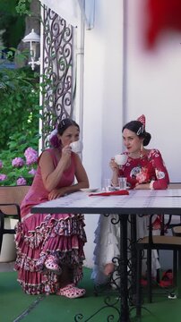 Two Spanish Flamenco Dancers in Colorful Traditional Costumes Relaxing in Historic Town Cafe During Cultural Festival