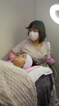 Cosmetologist performing high frequency facial treatment on client
