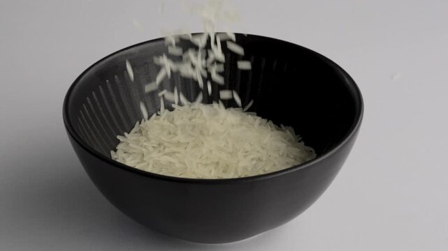 Raw white rice grains continuing to fill black bowl macro, FHD