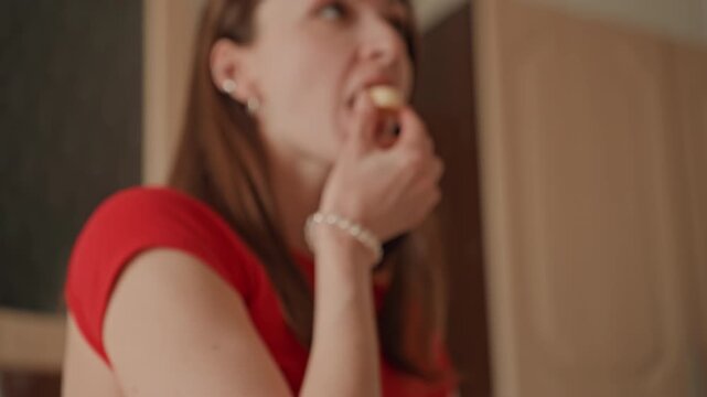 Woman home kitchen tasting small snack, contemplative portion control moment with clear container on countertop, casual red top, nutrition student role, mindful decision, warm indoor light, closeup