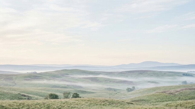 A serene landscape showcases rolling hills shrouded in a delicate mist. The distant mountains fade into a hazy horizon under a pale sky.