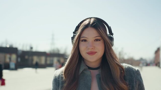 Chic young woman poses confidently on lively city street wearing stylish headset. Fashionable young lady stands confidently amidst city lights sporting modern headset with style and grace