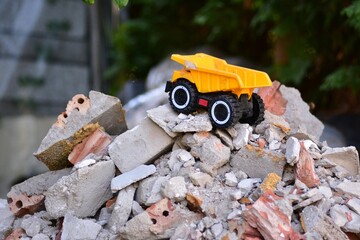 Yellow toy dump truck standing on a pile of broken concrete and bricks. Creative construction play concept with miniature heavy equipment surrounded by demolition rubble. © Karolina