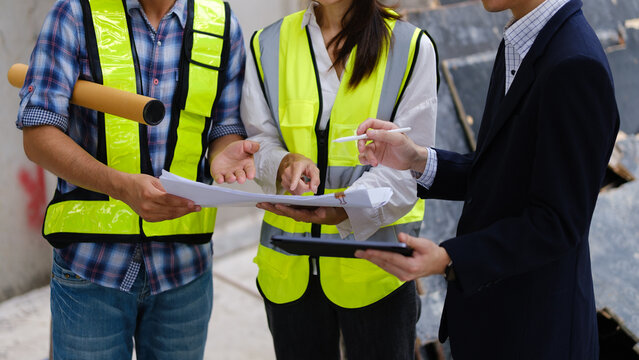 Architects and engineers reviewing blueprints and a scale model at a construction site.