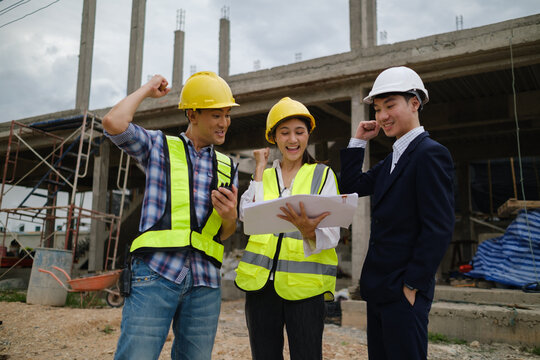 Construction team celebrating project progress while reviewing blueprints on site.