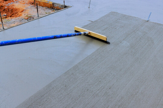 Workers smooth wet concrete at construction site using trowel on long handle