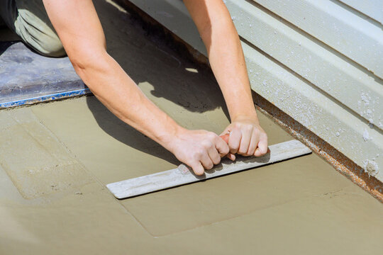 Worker levels concrete with trowel near building in construction setting